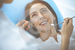 Smiling brunette woman being examined by dentist at dental clinic. Hands of a doctor holding dental instruments near