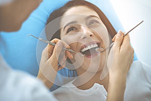 Smiling brunette woman being examined by dentist at dental clinic. Hands of a doctor holding dental instruments near