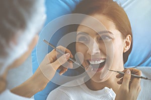 Smiling brunette woman being examined by dentist at dental clinic. Hands of a doctor holding dental instruments near