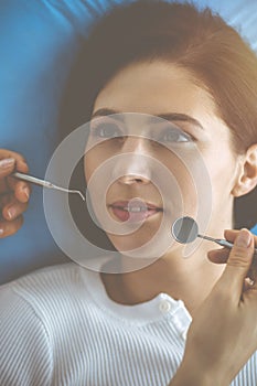 Smiling brunette woman being examined by dentist at dental clinic. Hands of a doctor holding dental instruments near