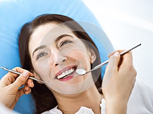 Smiling brunette woman being examined by dentist at dental clinic. Hands of a doctor holding dental instruments near