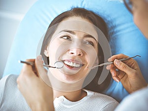 Smiling brunette woman being examined by dentist at dental clinic. Hands of a doctor holding dental instruments near