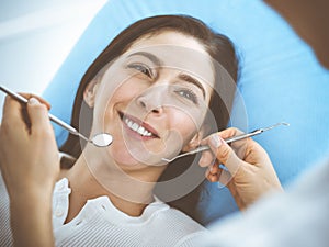 Smiling brunette woman being examined by dentist at dental clinic. Hands of a doctor holding dental instruments near