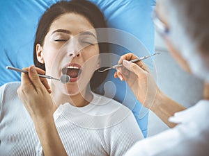 Smiling brunette woman being examined by dentist at dental clinic. Hands of a doctor holding dental instruments near