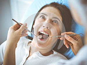 Smiling brunette woman being examined by dentist at dental clinic. Hands of a doctor holding dental instruments near