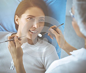 Smiling brunette woman being examined by dentist at dental clinic. Hands of a doctor holding dental instruments near