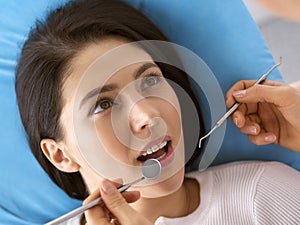 Smiling brunette woman being examined by dentist at dental clinic. Hands of a doctor holding dental instruments near