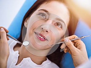 Smiling brunette woman being examined by dentist at sunny dental clinic. Hands of a doctor holding dental instruments