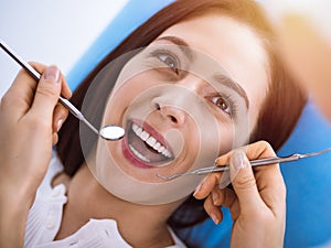 Smiling brunette woman being examined by dentist at sunny dental clinic. Hands of a doctor holding dental instruments