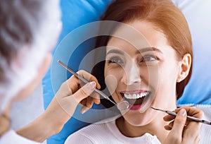 Smiling brunette woman being examined by dentist at sunny dental clinic. Hands of a doctor holding dental instruments