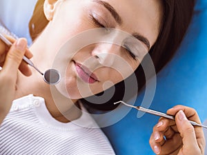 Smiling brunette woman being examined by dentist at sunny dental clinic. Hands of a doctor holding dental instruments