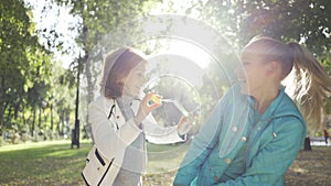 Smiling brunette woman blowing soap bubbles to her teenage granddaughter in the sunny autumn park. Happy family spending