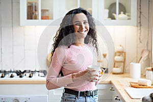 Smiling Brunette Woman With Cup Of Coffee In Hands Standing In Kitchen