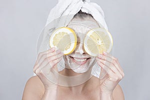 Smiling brunette woman holding two slice of lemon in front of her face. woman with moisturizing facial mask