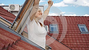 Smiling brunette woman opens attic window under the roof and stretches out hands