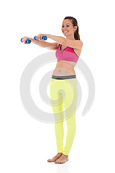 Smiling brunette woman in sports neon yellow leggings and pink bra doing complex exercises for muscles of hands using dumbbell