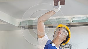 Smiling builder female in hardhat sanding wall indoors at construction site