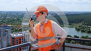 Smiling builder wearing construction uniform and safety helmet, holding walkie-talkie and talking. Business, building