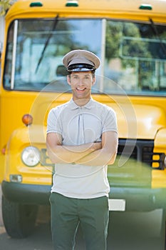 Smiling bus driver standing with arms crossed in front of bus