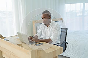 Smiling business black american man, African person working from home, using earphones to listen to music with computer notebook