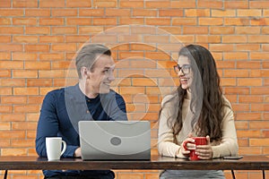 Smiling business blonde, white couple people working from home and talking together with computer notebook laptop and coffee on