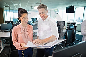 Smiling business colleagues discussing over clipboard at desk