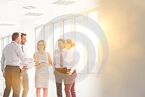 Smiling business colleagues discussing while standing in new office with yellow lens flare in background