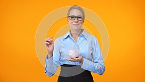 Smiling business lady putting coin piggybank bright background, bank deposit
