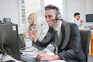 Smiling business man with headset working on desktop computer in customer service support center.