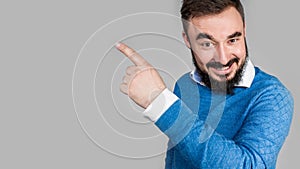 Smiling business man pointing left with index finger and looking at camera, isolated on gray background