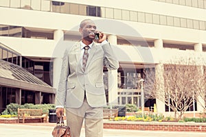 Smiling business man talking on mobile phone holding briefcase walking down the street