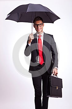 Smiling business man under an umbrella walking