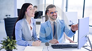 Smiling business man and woman sitting at a table and discussing project on computer at office.