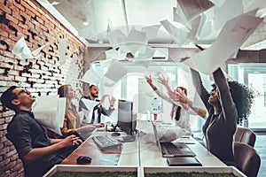 Smiling business people having fun by throwing papers in the air celebrating business success in the modern office