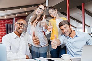 Smiling business people showing thumbs up working in office
