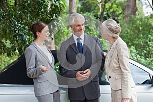 Smiling business people talking together by classy cabriolet