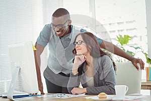 Smiling business professionals looking at computer while working at desk