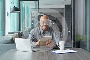 Smiling business senior old elderly black american man, African person working from home on table with tablet and notebook