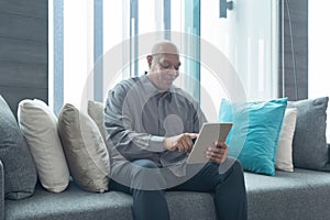 Smiling business senior old elderly black american man, African person working from home on tablet on sofa in quarantine in corona