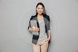 Smiling business woman with arm in pocket holding laptop computer