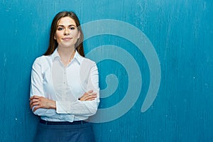 Smiling business woman with crossed arms portrait on blue wall.