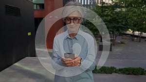 Smiling business woman elderly Caucasian mature businesswoman walking in city downtown outside texting sms messages