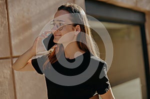 Smiling business woman in eyeglases is talking mobile phone while standing on building background