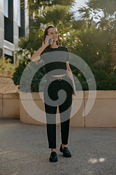 Smiling business woman in eyeglases is talking mobile phone while standing on building background