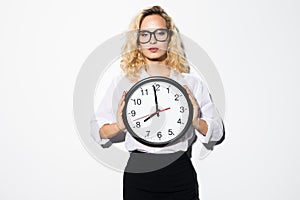 Smiling business woman in eyeglasses holding clock and looking at the camera over gray background