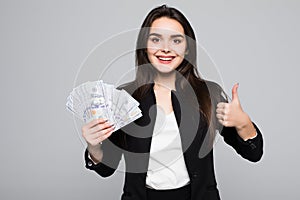 Smiling business woman holding money with thumbs up over gray background
