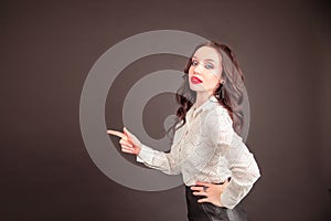 Smiling business woman pointing away while looking at the camera over gray background