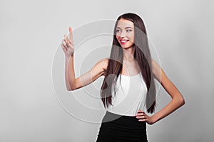 Smiling business woman pointing up and looking at the camera over gray background