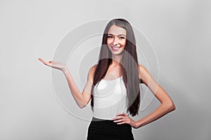 Smiling business woman pointing up and looking at the camera over gray background