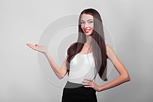 Smiling business woman pointing up and looking at the camera over gray background